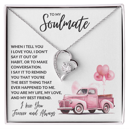 A necklace with a gold finish, featuring a heart-shaped pendant with a central cubic zirconia, surrounded by smaller crystals. The necklace is presented in a gift box with a quote and a pink car image, indicating it is a romantic gift.